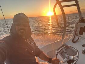 A fisherman captures a selfie while navigating his boat at sunset, showcasing the serene beauty of the ocean and the thrill of fishing adventures.