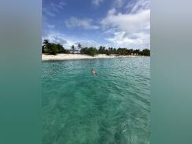 A person enjoys a refreshing swim in the crystal-clear waters of a tropical beach, surrounded by lush greenery and soft sand — a perfect getaway for relaxation and fun in the sun.
