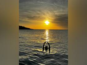 A silhouette of a person swimming at sunset, forming a heart shape with their hands — a romantic and picturesque moment on the water.