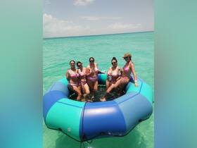 A fun group of friends enjoys drinks while floating in a vibrant inflatable in crystal-clear waters, perfect for a summer getaway or celebration.