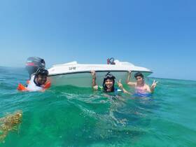 A joyful group enjoys snorkeling in clear waters, posing with their boat while having fun under the sun — a perfect day for aquatic adventures.