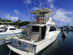 A stunning view of the 'Real Life' yacht docked in a marina, showcasing its sleek design against a backdrop of clear blue skies and palm trees — perfect for fishing charters in Honolulu, Hawaii.