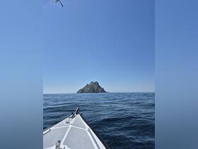 A stunning view of a rocky island from the bow of a boat, showcasing the beauty of the open sea and clear skies — perfect for adventure seekers and nature lovers.