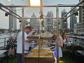 Guests enjoy a buffet spread on a boat, featuring a variety of dishes against a stunning city backdrop — perfect for dining experiences on the water.