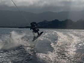 A wakeboarder catches air while being towed across the water, showcasing thrilling water sports action against a scenic backdrop.