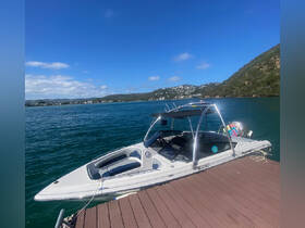 A sleek speedboat docked at a scenic waterfront, showcasing its modern design against a backdrop of lush hills and clear blue skies.