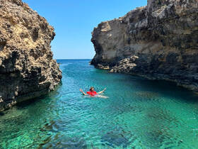 A person enjoys a refreshing swim in crystal-clear waters surrounded by stunning rock formations, showcasing the beauty of a hidden cove.