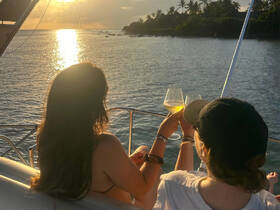 Two friends toast with cocktails against a stunning sunset backdrop while enjoying their time on a boat — a perfect moment for celebration and relaxation on the water.