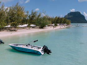 A speedboat named 'Sun Chaser 2' is docked in clear turquoise waters, with a scenic beach and lush greenery in the background, perfect for a day of relaxation and adventure.