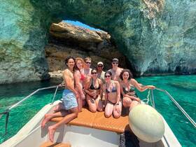 A cheerful group poses on the deck of a boat near a stunning rock formation, enjoying a sunny day on the water — perfect for summer adventures and memorable outings.