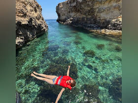 A person floats in crystal-clear waters surrounded by rocky cliffs, showcasing a perfect summer day for swimming and relaxation.