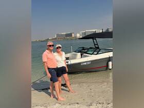 A cheerful couple poses on the beach beside their boat, enjoying a sunny day by the water — perfect for memorable outings and adventures.