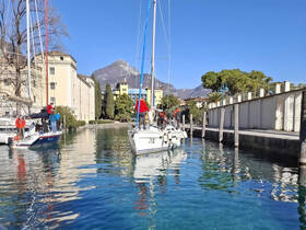 A group of sailors prepares their boats in a picturesque marina, surrounded by stunning mountain views — perfect for a day of sailing adventures.