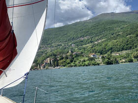 A picturesque view of a sailboat navigating a serene lake, surrounded by lush mountains and charming villages — an ideal setting for a sailing adventure.