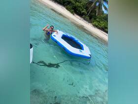 A woman enjoys a sunny day in the clear waters, posing with a peace sign next to an inflatable float — a perfect moment of fun and relaxation at the beach.