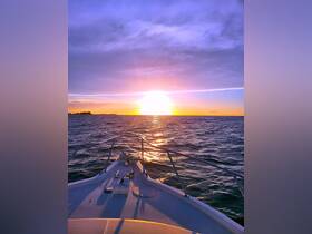 A stunning sunset view from the bow of a boat, casting golden reflections on the water — perfect for evening cruises and serene moments on the sea.