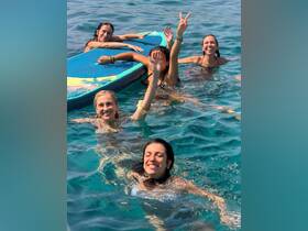 A lively group of friends enjoys a fun day in the water, swimming and posing with a paddleboard — perfect for summer adventures and memorable outings.