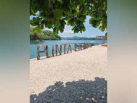 A scenic view of the Punta Cernia sign on the beach, framed by lush greenery and a tranquil water backdrop, perfect for showcasing beautiful destinations.