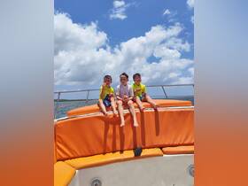 Three kids enjoy snacks on the deck of a boat under a sunny sky, capturing a joyful family moment on the water.