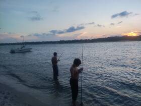 Two boys enjoy fishing at sunset along the shoreline, with a boat anchored nearby — a perfect scene for family bonding and outdoor adventures.