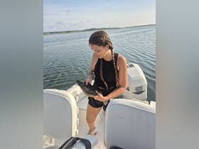 A woman proudly holds her catch while fishing on a boat, showcasing the thrill of the fishing experience on the water.