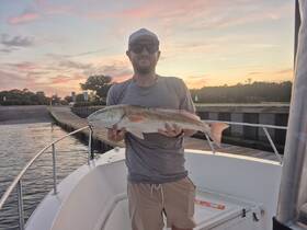 A proud angler holds up a freshly caught fish against a stunning sunset backdrop, showcasing the thrill of fishing adventures on the water.