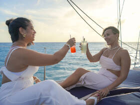 Two friends toast with cocktails aboard a yacht at sunset, capturing the essence of celebration and relaxation on the water.