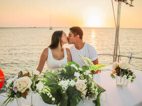A couple shares a romantic kiss at sunset aboard a yacht, surrounded by beautiful floral arrangements — an ideal setting for intimate dinner cruises or special celebrations.
