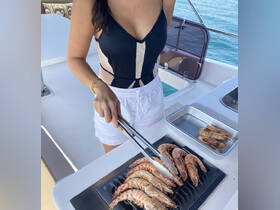 A woman prepares fresh shrimp on the grill aboard a yacht, showcasing the perfect amenities for a luxurious dining experience on the water.