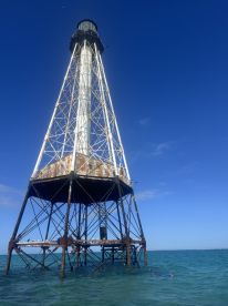 A lighthouse stands tall above the water, showcasing its structure against a clear blue sky. Ideal for maritime photography enthusiasts.