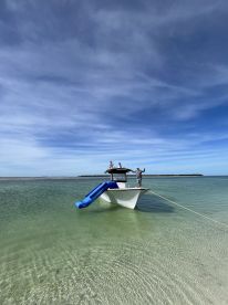 A group enjoys a fun day at the sandbar, with a boat featuring a slide for water activities — perfect for summer adventures on the water.