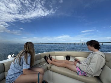 Two young individuals relax on a boat, enjoying the scenic view of a bridge over the water — a perfect moment for a day out on the water.