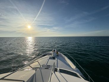 A serene sunset view from the bow of a boat, capturing the tranquil ocean and a guest enjoying the moment — perfect for sunset cruises.