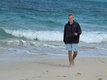 A teenager walks along the beach, enjoying the ocean waves — a perfect moment of relaxation and fun by the water.