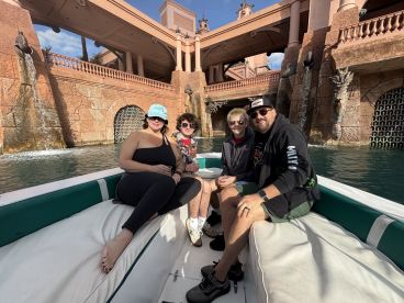 A cheerful group enjoys a boat ride, surrounded by stunning architecture and water features — perfect for a memorable vacation experience.