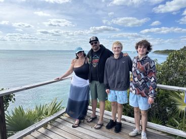 A family poses together on a scenic overlook by the ocean, capturing a memorable moment during their trip — perfect for family vacations and coastal adventures.