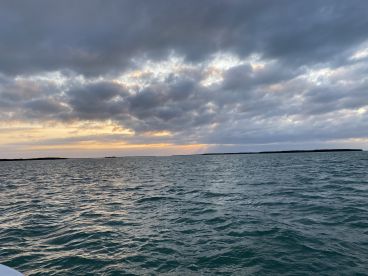 A stunning sunset over the water, with dramatic clouds and a distant coastline, perfect for capturing the beauty of a tranquil evening on the water.