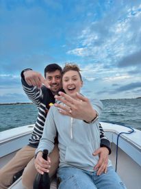 A joyful couple celebrates their engagement on a boat, showcasing the ring and capturing a memorable moment on the water.