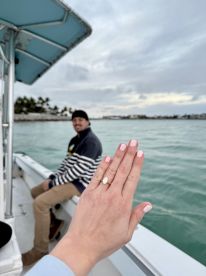 A joyful moment captured on a boat as a couple celebrates their engagement, showcasing the stunning ring against a beautiful water backdrop.