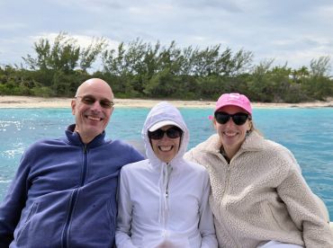 A cheerful group enjoys a boat ride, smiling against a backdrop of turquoise waters and a sandy beach — perfect for family adventures in the Bahamas.
