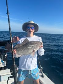 A young man proudly holds up his catch while fishing on the open ocean, showcasing the excitement of a successful day on the water.