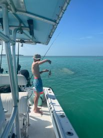 A young man enjoys a day of fishing on a boat, showcasing his catch against the stunning turquoise waters — a perfect moment for fishing enthusiasts.