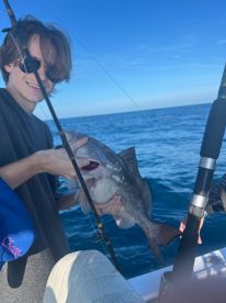 A young angler proudly holds up his catch while fishing in the open ocean, showcasing the thrill of a successful day on the water.