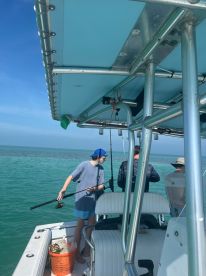 A group of individuals enjoys a fishing trip on a boat, with one person preparing to cast their line into the clear blue waters — a perfect day for ocean adventures.