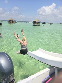 A joyful moment captured as a woman jumps into the clear waters, surrounded by friends and boats, highlighting the fun of a sandbar stop.