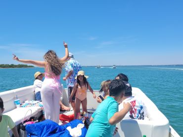 A lively group enjoys a fun day on the water, dancing and celebrating aboard a boat under the bright sun — perfect for family outings and summer adventures.