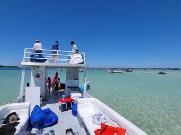 A lively group enjoys a day on the water, with children and adults engaging in activities aboard the boat, surrounded by clear turquoise waters and other vessels.