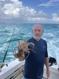 A man proudly displays his catch of the day, a large lobster, while out fishing on the open ocean — a thrilling experience for seafood lovers.