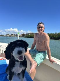 A man enjoys a sunny day on the boat with his cheerful dog, capturing a moment of relaxation and companionship on the water.