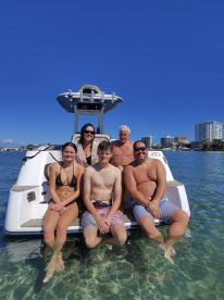 A joyful family poses on the back of a boat, enjoying a sunny day in clear waters — perfect for creating lasting memories on the water.